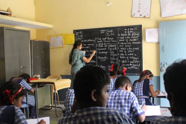 A teacher writing on the blackboard while children work in a classroom